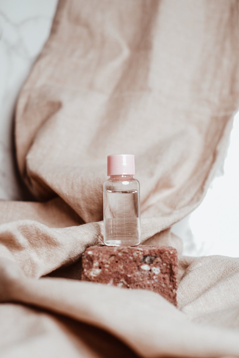 Transparent Cosmetic Bottle on Rock with Brown FAbric on Background